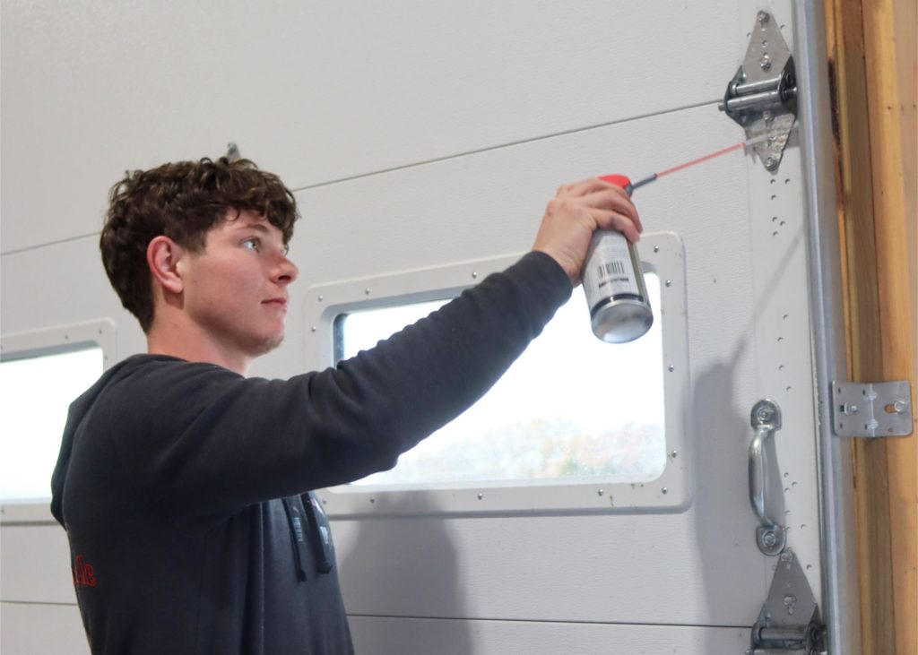 A technician lubricating overhead door hinges in southwest Missouri