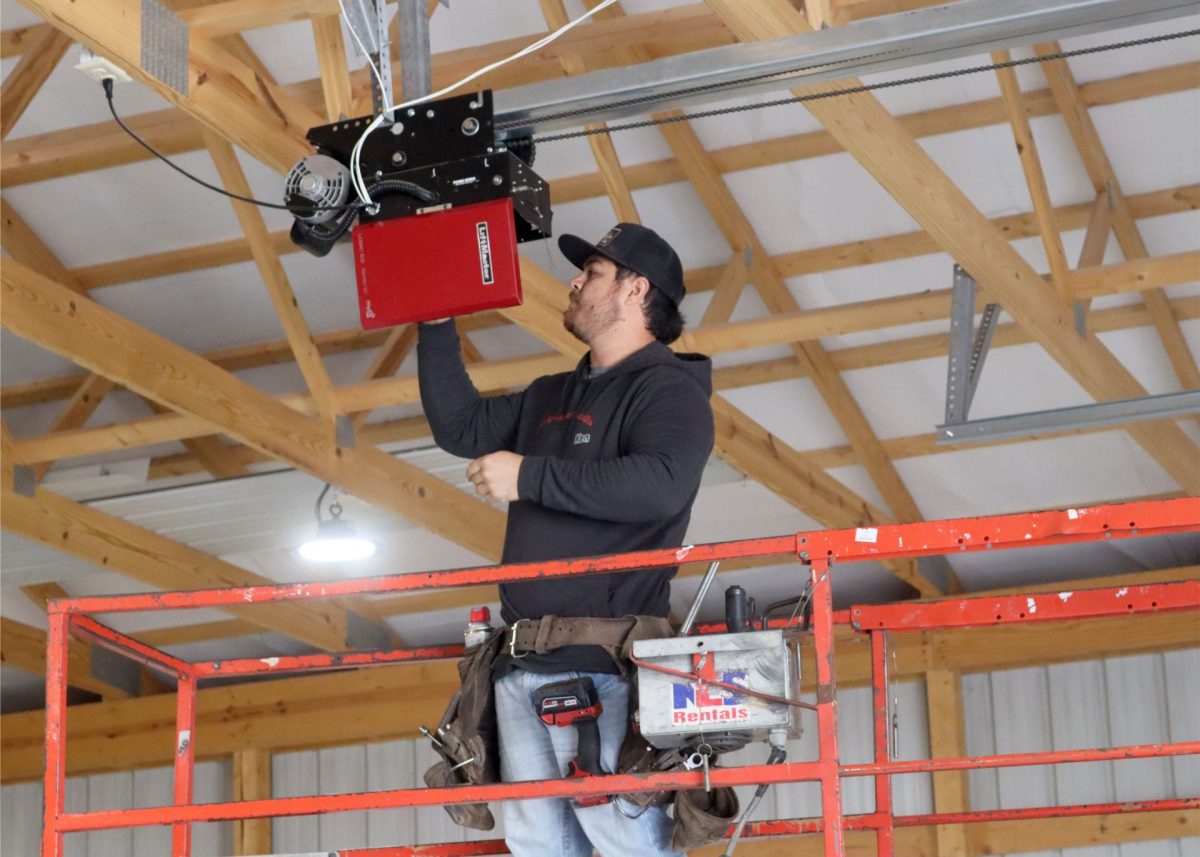 An overhead door technician in a scissor lift servicing an commercial Liftmaster opener near Springfield, Missouri